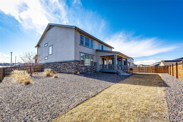 back of property with stone siding and a fenced backyard