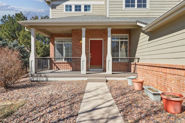 doorway to property featuring roof with shingles, a porch, and brick siding