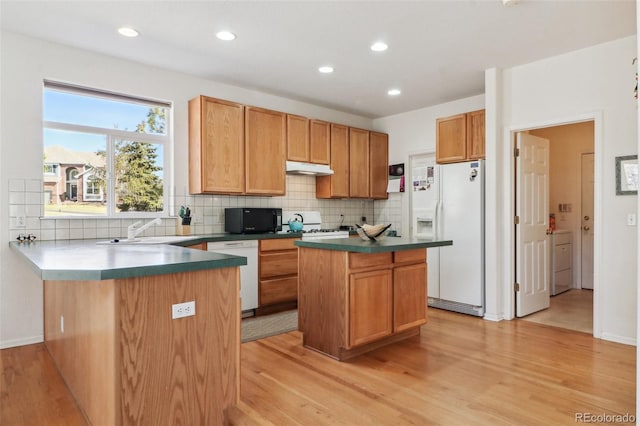 kitchen featuring a peninsula, white appliances, light wood finished floors, and a sink