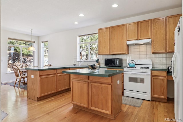 kitchen with dark countertops, white appliances, under cabinet range hood, and decorative backsplash