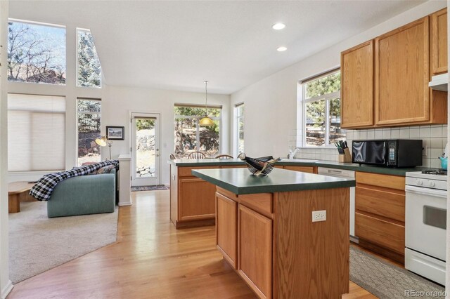 kitchen with dark countertops, a center island, white gas range, black microwave, and backsplash