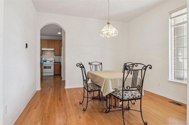 dining area with light wood-type flooring, a wealth of natural light, visible vents, and arched walkways