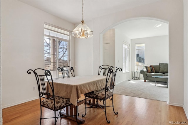 dining space featuring arched walkways, a notable chandelier, baseboards, and wood finished floors