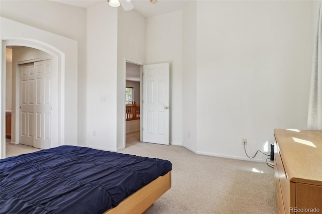 bedroom featuring baseboards, arched walkways, a towering ceiling, and light colored carpet