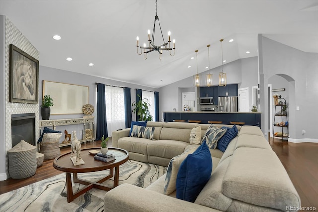 living room with a chandelier, dark hardwood / wood-style flooring, vaulted ceiling, and a tiled fireplace