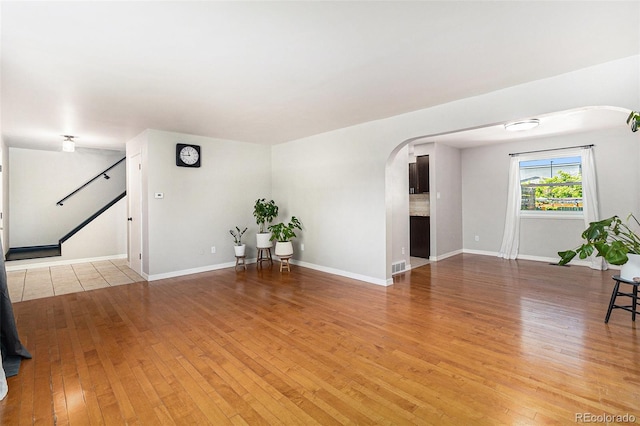 6731 Devinney St, Arvada, CO 80004 - unfurnished living room featuring arched walkways, light wood-style flooring, stairs, and baseboards