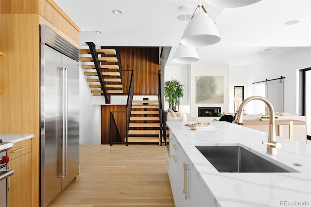 kitchen featuring built in fridge, a sink, light wood-style flooring, light stone countertops, and modern cabinets