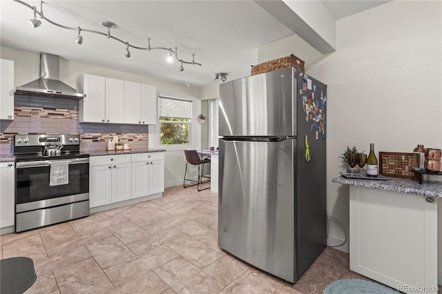 kitchen featuring tasteful backsplash, stainless steel appliances, wall chimney range hood, dark stone countertops, and white cabinets