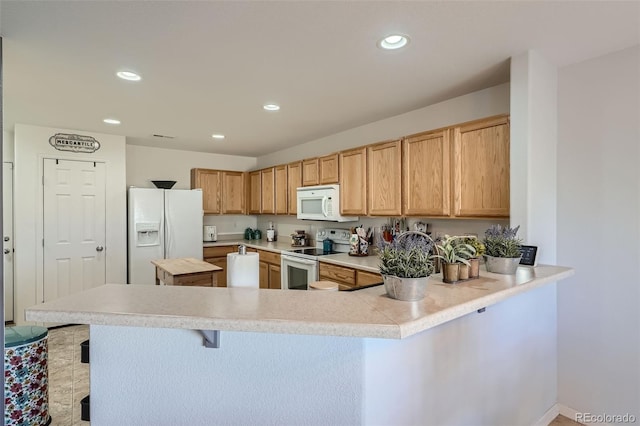 kitchen with kitchen peninsula, light brown cabinets, white appliances, and a breakfast bar area