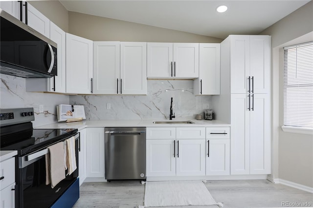 kitchen featuring tasteful backsplash, lofted ceiling, appliances with stainless steel finishes, white cabinetry, and a sink