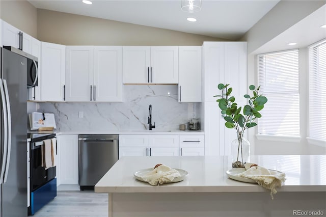 kitchen with lofted ceiling, a sink, light countertops, white cabinets, and appliances with stainless steel finishes