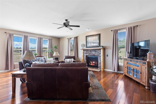 living room with a stone fireplace, dark wood-type flooring, and a wealth of natural light