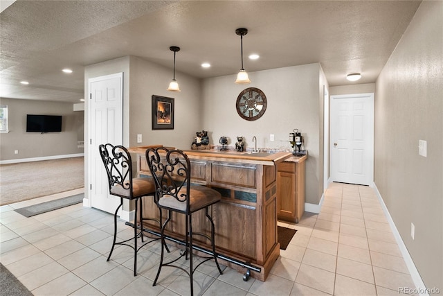 bar featuring pendant lighting, light tile patterned floors, sink, and a textured ceiling