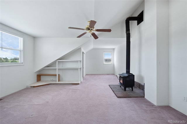 additional living space featuring light colored carpet, ceiling fan, and a wood stove