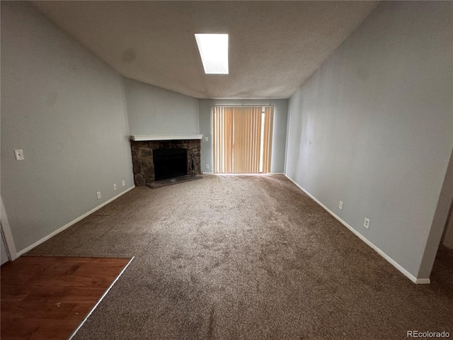 unfurnished living room with lofted ceiling with skylight, a stone fireplace, carpet floors, and a textured ceiling