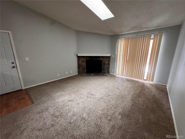 unfurnished living room featuring a stone fireplace, carpet, a textured ceiling, and a skylight