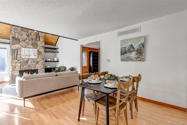 dining space with a stone fireplace, wood-type flooring, and a textured ceiling