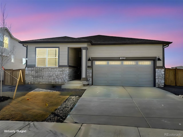 view of front facade featuring a garage, driveway, stone siding, and fence