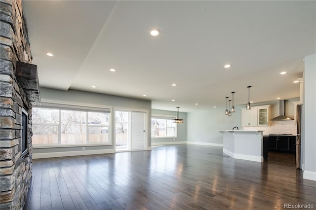 unfurnished living room with dark wood-type flooring and a stone fireplace