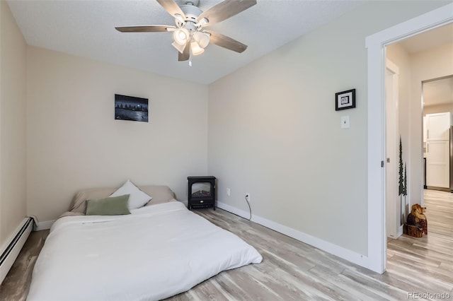 3144 S Wheeling Way Unit 401, Aurora, CO 80014 - bedroom with baseboard heating, light wood-style floors, a wood stove, baseboards, and ceiling fan