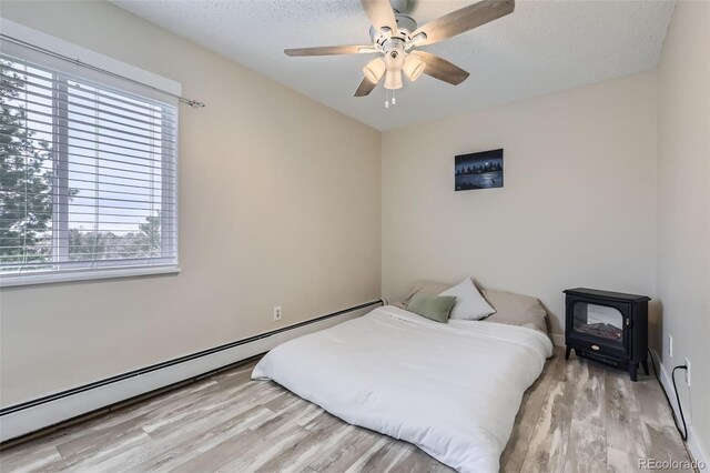 3144 S Wheeling Way Unit 401, Aurora, CO 80014 - bedroom featuring baseboard heating, wood finished floors, a wood stove, a textured ceiling, and a ceiling fan
