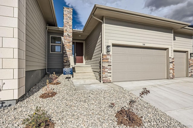 view of front of house with entry steps, concrete driveway, a chimney, and an attached garage