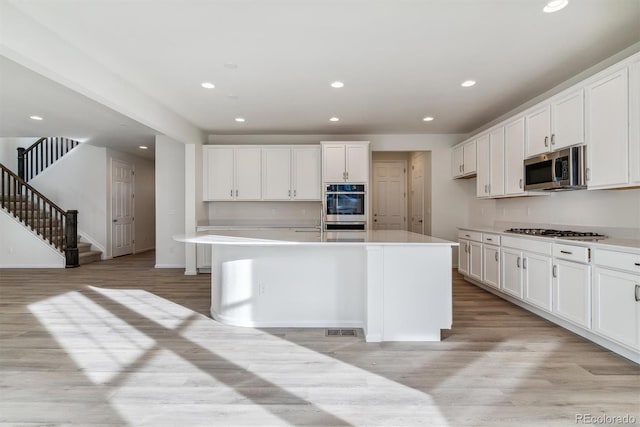 kitchen with a center island with sink, light wood-type flooring, white cabinetry, and stainless steel appliances