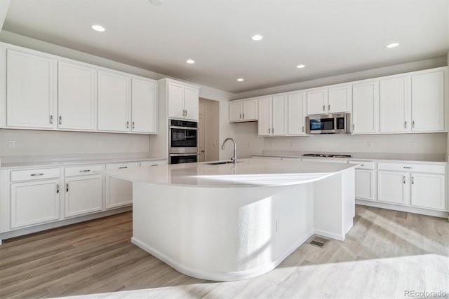 kitchen featuring white cabinets, sink, light hardwood / wood-style flooring, an island with sink, and stainless steel appliances