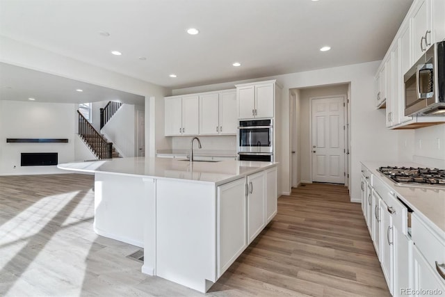 kitchen featuring white cabinetry, sink, stainless steel appliances, light hardwood / wood-style flooring, and a center island with sink