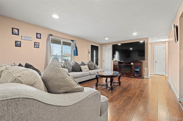 living area with recessed lighting, a glass covered fireplace, hardwood / wood-style flooring, and baseboards