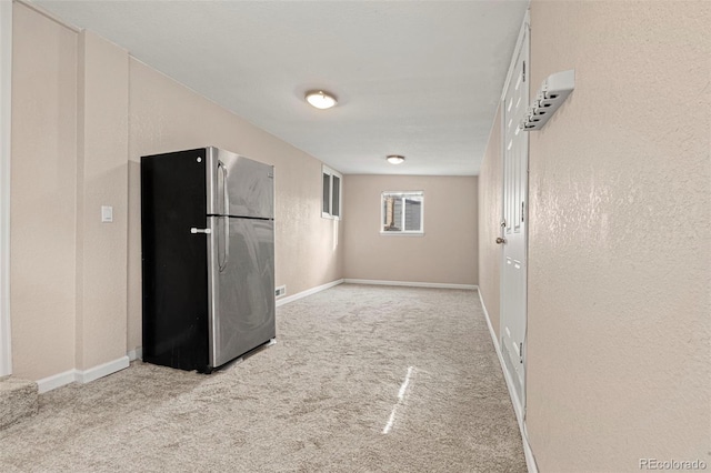 interior space featuring carpet flooring, a textured wall, and baseboards