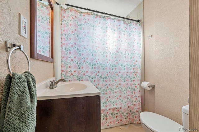 full bathroom with tile patterned flooring, a textured wall, vanity, and toilet