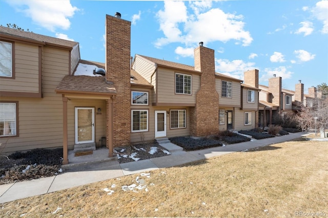 rear view of property featuring entry steps, a shingled roof, a chimney, and a lawn