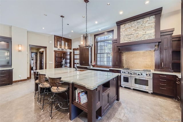kitchen with double oven range, tasteful backsplash, light stone counters, a center island with sink, and a kitchen breakfast bar