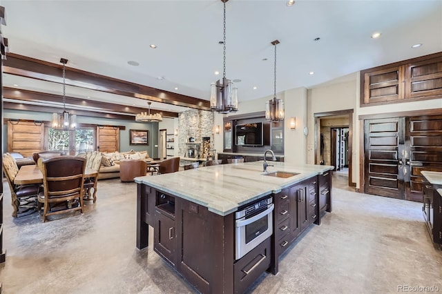 kitchen with a sink, a chandelier, hanging light fixtures, light stone counters, and open floor plan