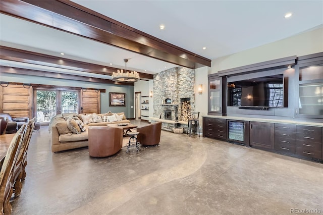 living room featuring a stone fireplace, a chandelier, bar, beverage cooler, and beam ceiling