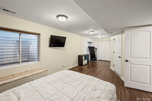 bedroom with dark wood-style floors, baseboards, visible vents, and a textured ceiling