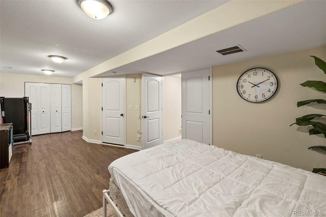 bedroom with dark wood-type flooring, visible vents, a textured ceiling, and baseboards