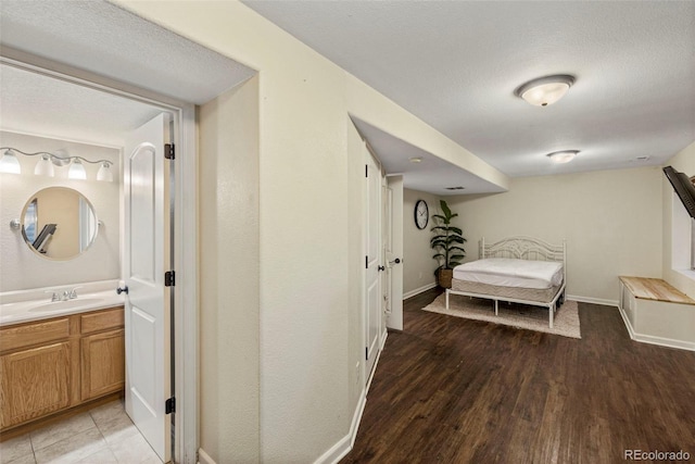 hallway featuring light wood-type flooring, a textured ceiling, baseboards, and a sink