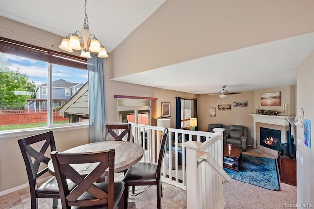 dining area with a tiled fireplace, ceiling fan with notable chandelier, and vaulted ceiling