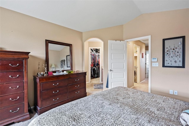 bedroom with lofted ceiling, washer / dryer, a spacious closet, light colored carpet, and a closet