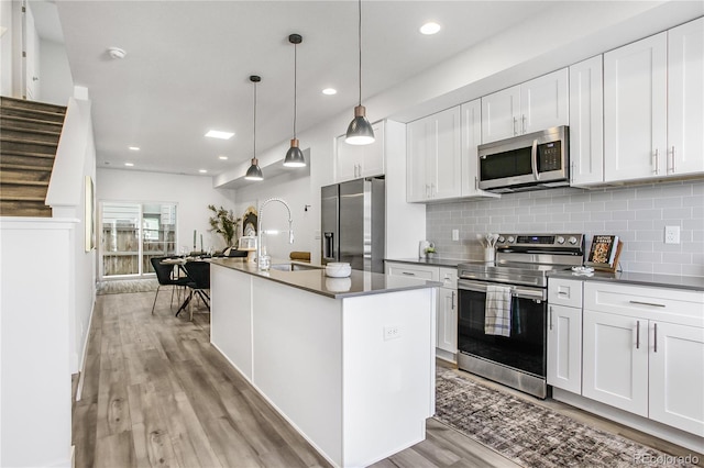 kitchen with a sink, backsplash, open floor plan, stainless steel appliances, and light wood finished floors