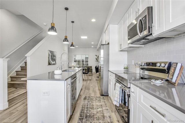 kitchen with light wood finished floors, tasteful backsplash, appliances with stainless steel finishes, white cabinets, and a sink