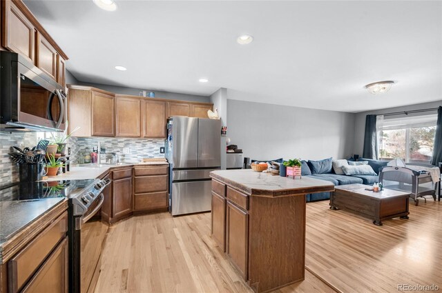 kitchen featuring decorative backsplash, stainless steel appliances, a kitchen island, and light wood-style floors