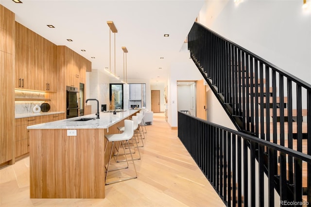 kitchen with a kitchen breakfast bar, pendant lighting, a large island, sink, and light stone counters