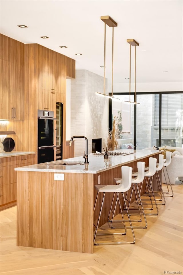 kitchen with light hardwood / wood-style flooring, double oven, decorative light fixtures, sink, and a breakfast bar area