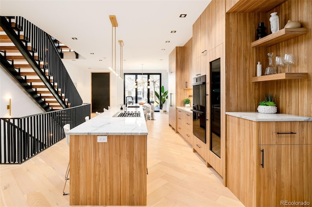 kitchen with a center island, decorative light fixtures, double oven, sink, and light stone counters