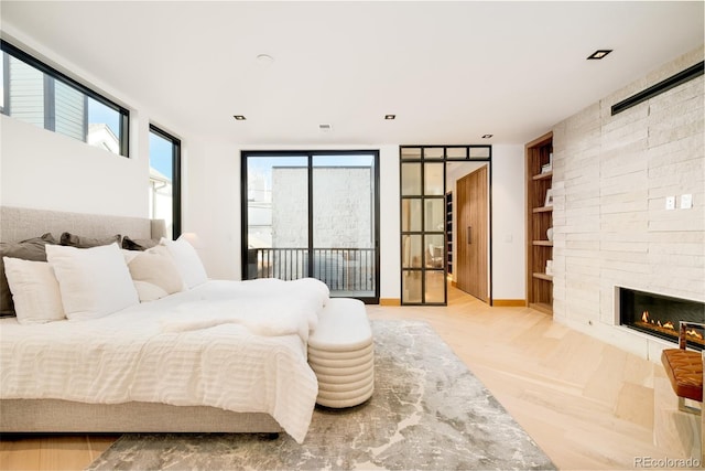 bedroom with a stone fireplace, access to outside, and light parquet flooring