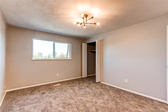 unfurnished bedroom featuring a textured ceiling, carpet, and a notable chandelier