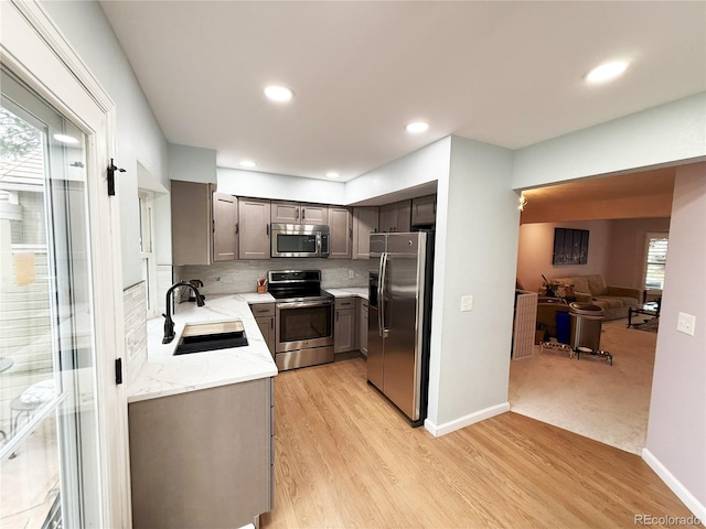 kitchen with backsplash, sink, light hardwood / wood-style flooring, light stone counters, and stainless steel appliances